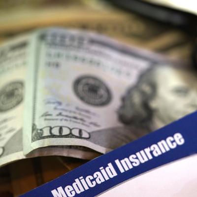 Medicaid Insurance label strewn across a stack of hundred dollar bills